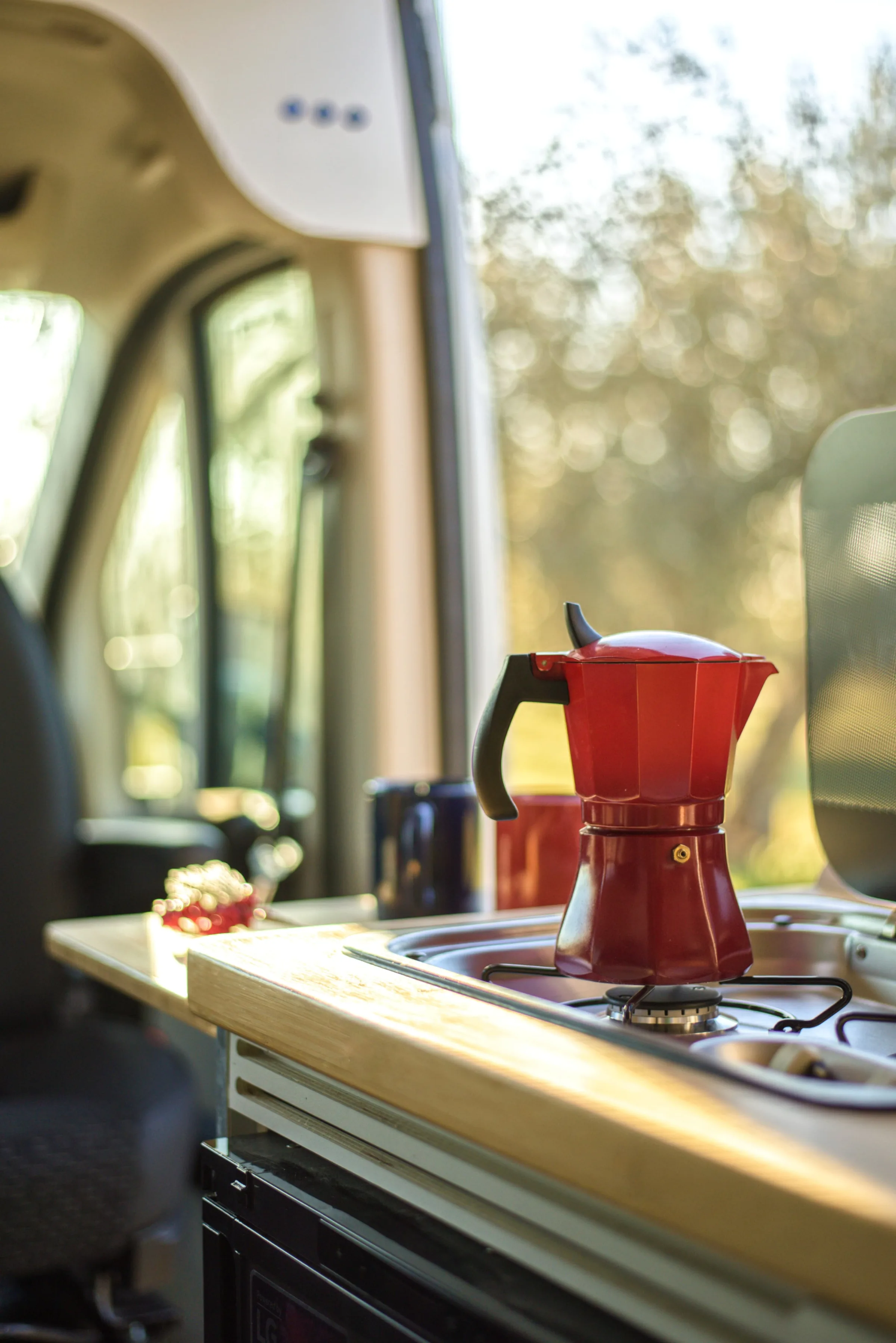 Cafetera italiana roja sobre la encimera de una camper Alquicamper con luz dorada