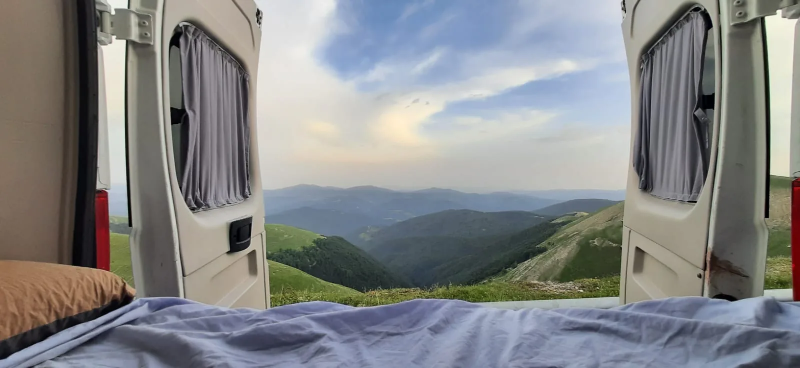 Vista desde la cama de una camper Alquicamper hacia un valle de montañas en Europa · seguro toda la UE incluido