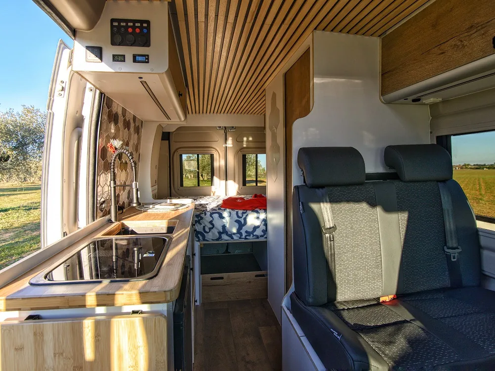 Interior camperizado completo: cocina, salón con asientos giratorios y cama trasera · camperización propia de Alquicamper