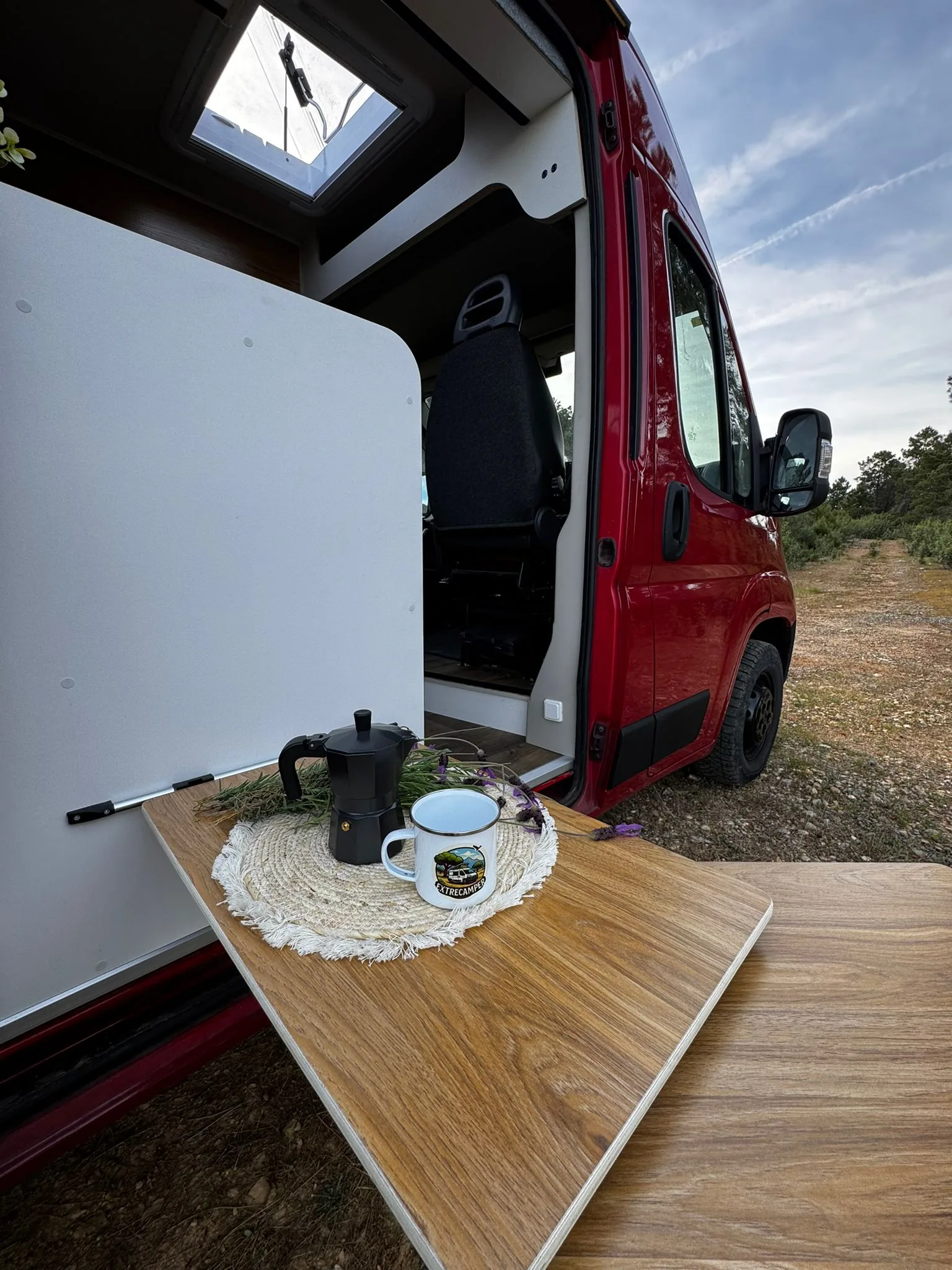 Mesa exterior de una camper Alquicamper con cafetera, taza y mochila al atardecer