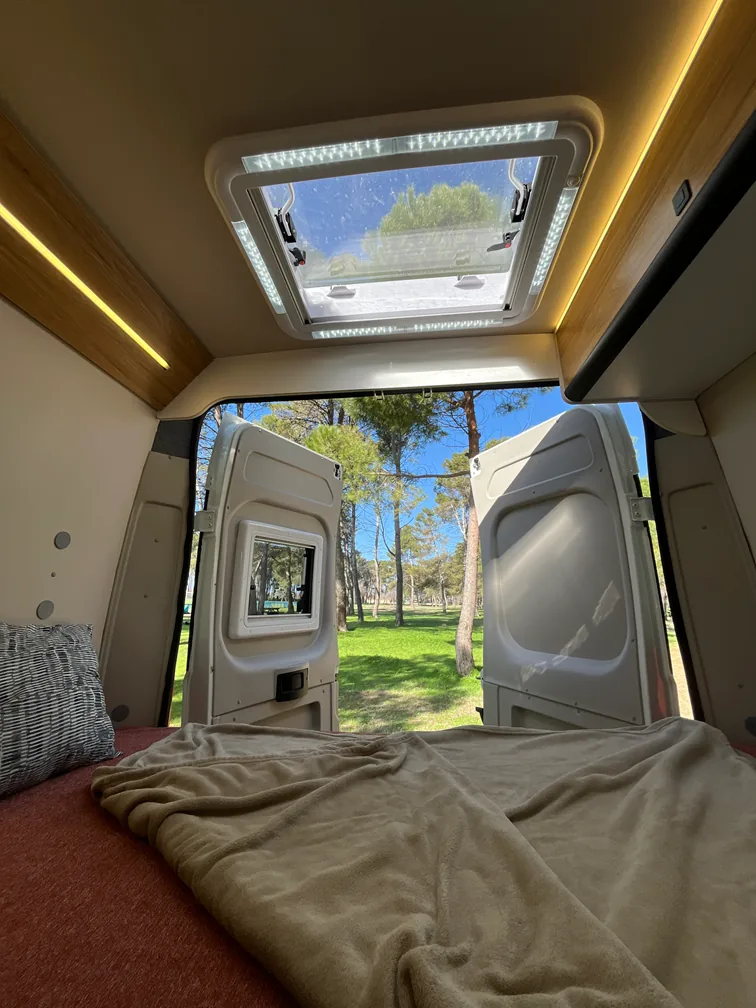 Cama de una furgoneta camper con las puertas traseras abiertas a la naturaleza al amanecer