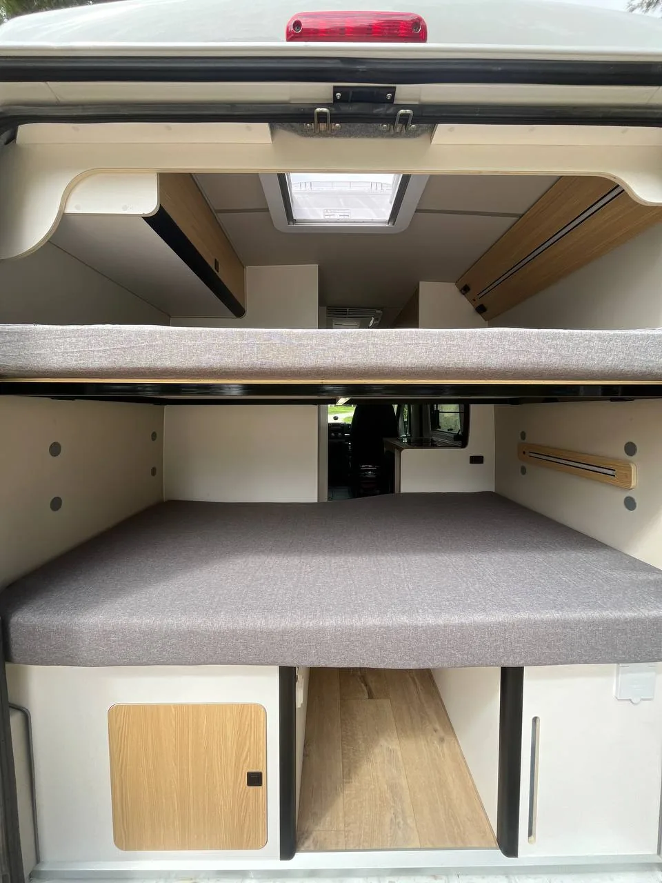 Cama trasera de una camper Alquicamper con las puertas traseras abiertas · interior listo para dormir